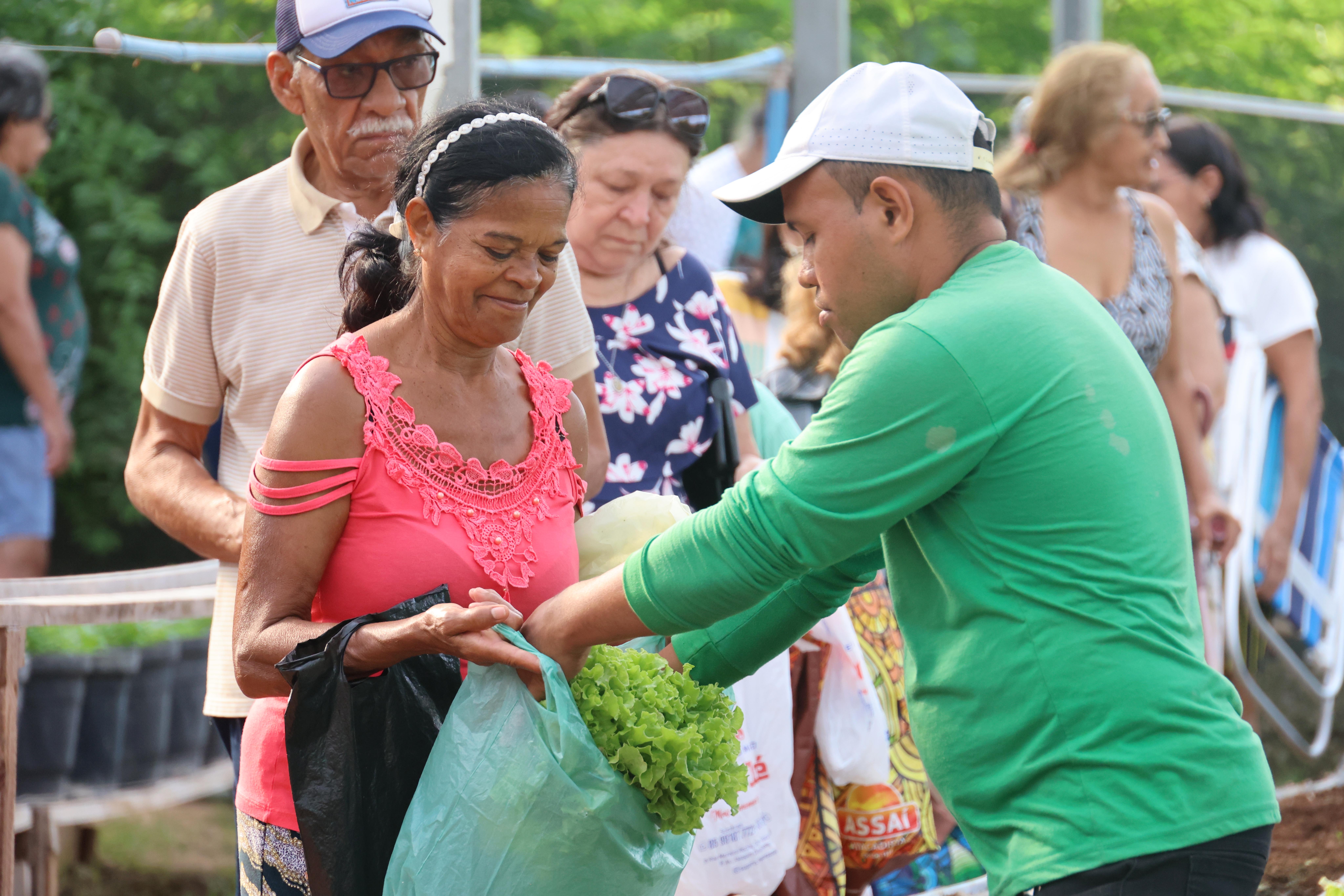 homem colocando verduras na sacola de uma idosa atendida pela horta social